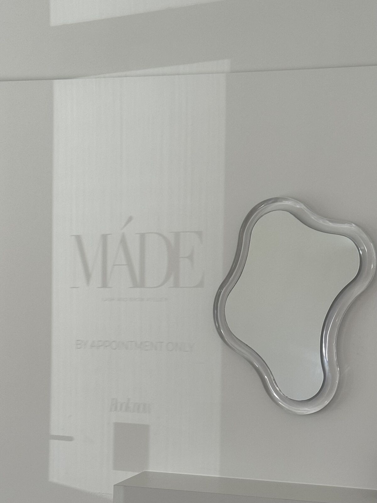The MÁDE studio window, lettered by appointment only, beside a wavy-edged mirror
